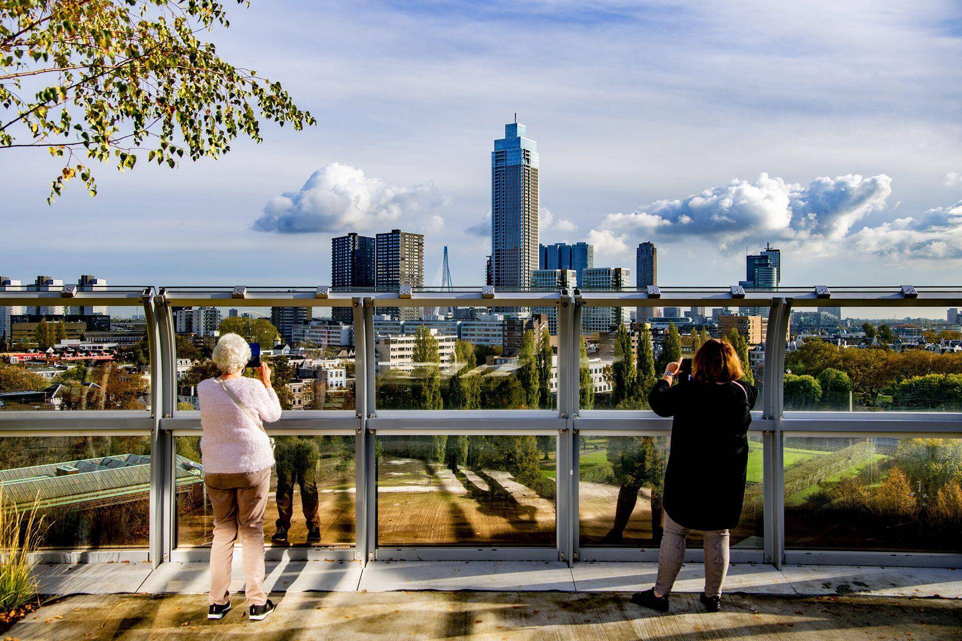 Op de foto zijn twee mensen te zien die vanaf een hoger gelegen punt uitkijken over de stad Rotterdam.