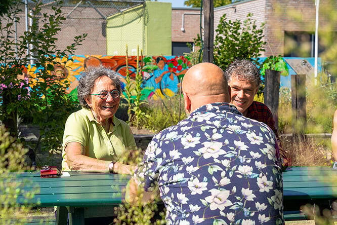 Drie mensen met elkaar in gesprek een een tuintafel