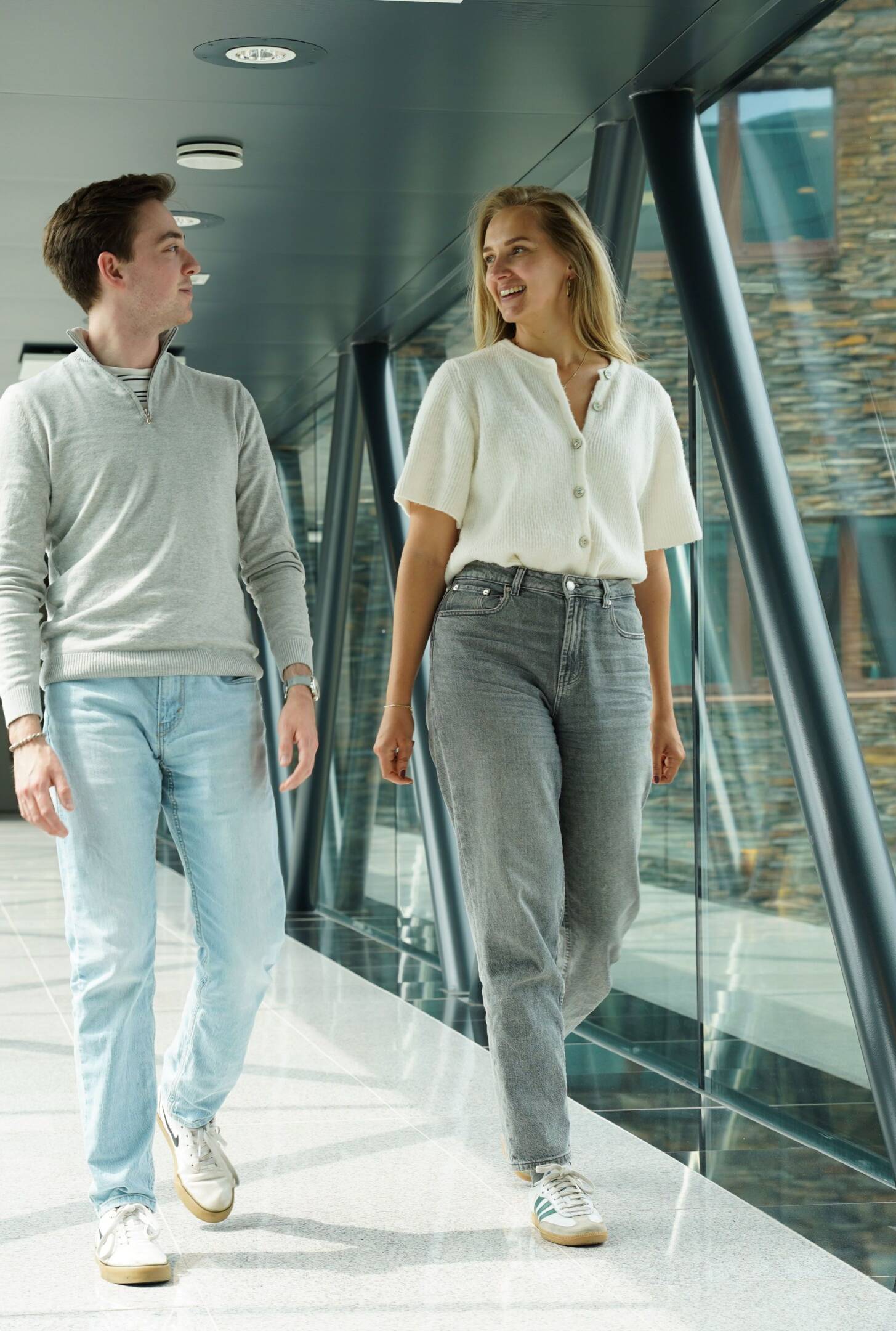 Een man en een vrouw lopen op een loopbrug en kijken elkaar glimlachend aan.
