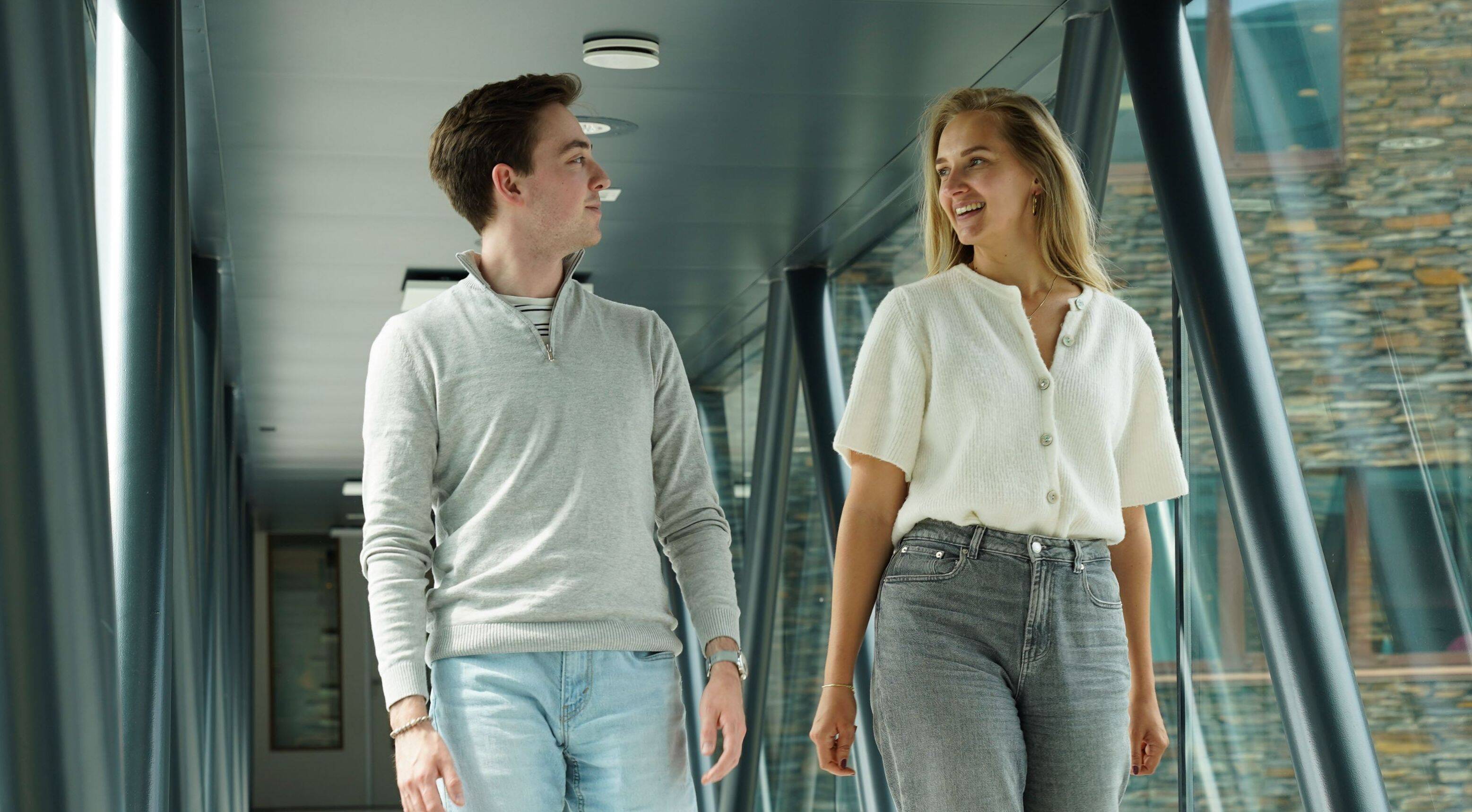Een man en een vrouw lopen op een loopbrug en kijken elkaar glimlachend aan.
