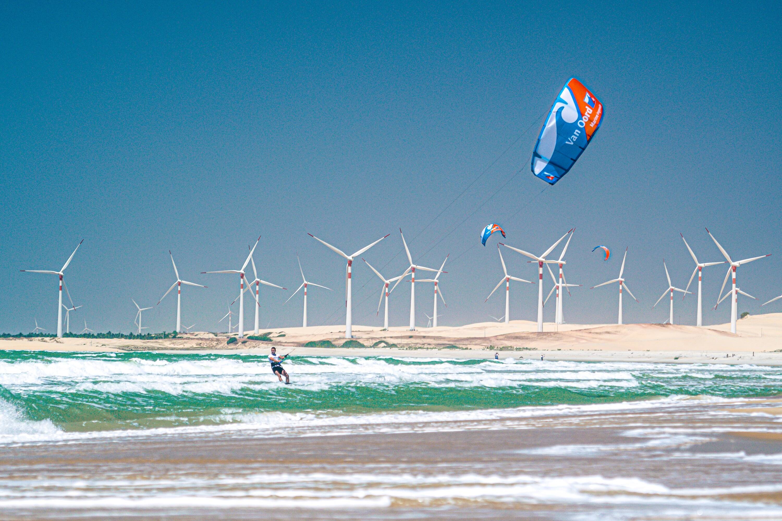 Person kitsurfing in front a a large array of electric windmills