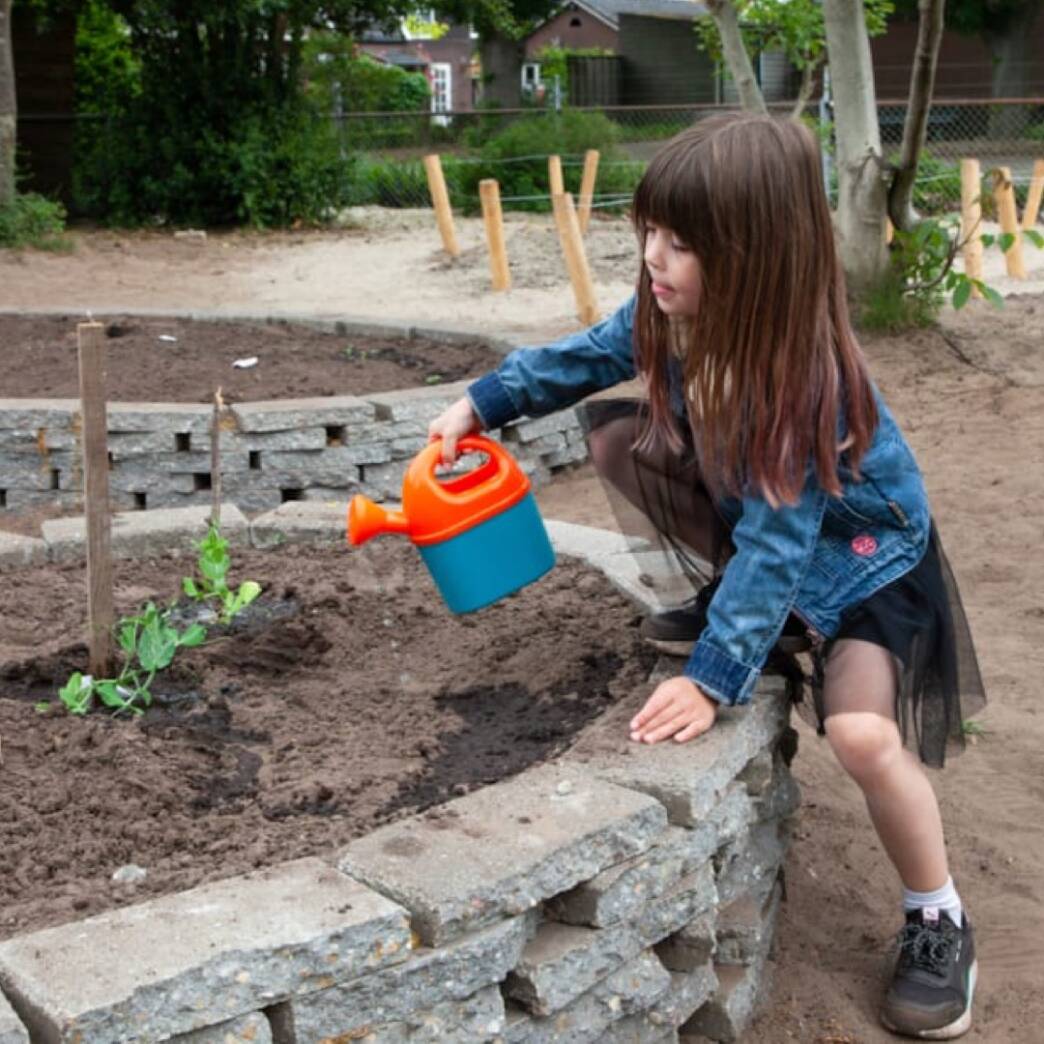 Op de foto staat een meisje die een plant water geeft.